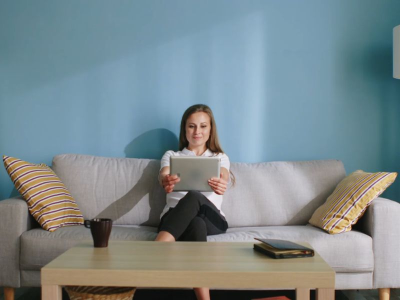 devojka sedi na maloj ugaonoj sive boje i koristi tablet