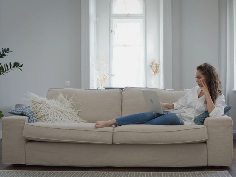 devojka leži na ugaonoj garnituri i koristi laptop