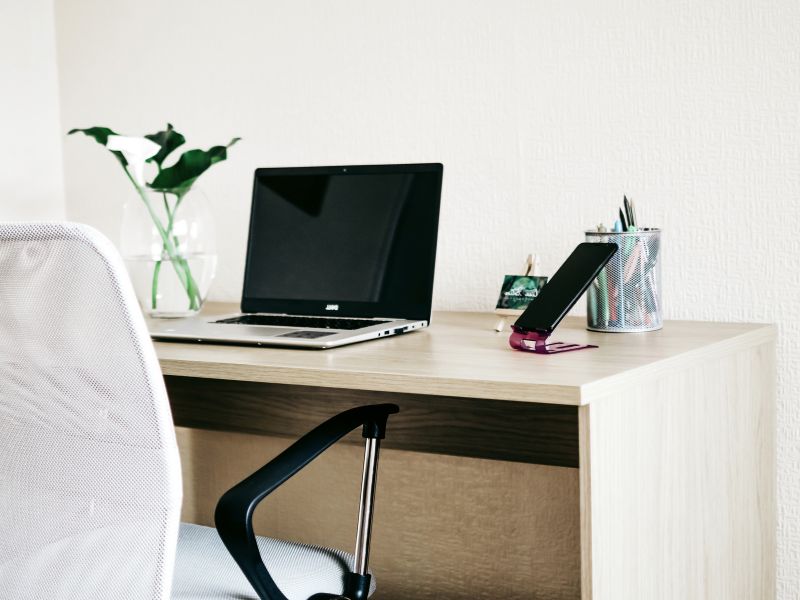 adni sto od svetlog drveta sa laptopom, ergonomskom stolicom i kancelarijskim nameštajem u kućnom okruženju.